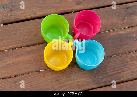 Blu, rosa, verde e giallo tazze di stare a cerchio sul tavolo di legno Foto Stock