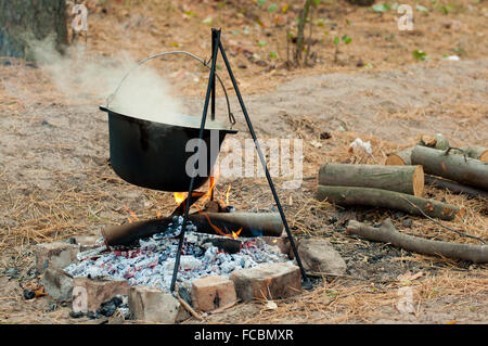 La cottura di porridge in pot nero sul fuoco in foresta Foto Stock