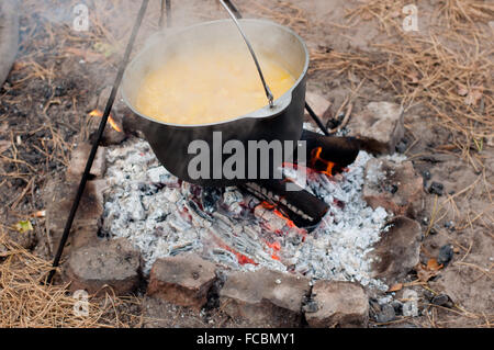 La cottura di porridge in pot nero sul fuoco in foresta Foto Stock