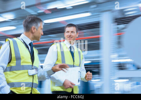 Uomini d'affari in abbigliamento riflettivo camminare e parlare in fabbrica Foto Stock
