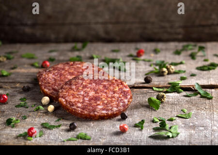 Fette di salame con prezzemolo e pepe su sfondo di legno Foto Stock