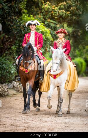 Lusitano. Matura in costumi barocchi su una baia e grigio stallone trotto su un percorso di giardino. Portogallo Foto Stock