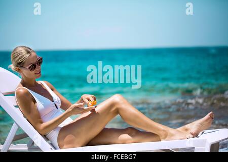 Giovane donna l'applicazione di crema solare su una sedia a sdraio. Foto Stock