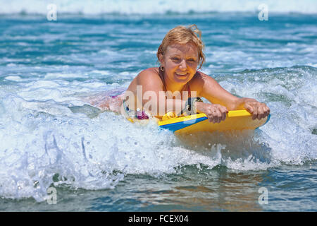 Gioiosa la mezza età della donna - surfer con bodyboard surf con il divertimento sulle piccole onde del mare. Foto Stock