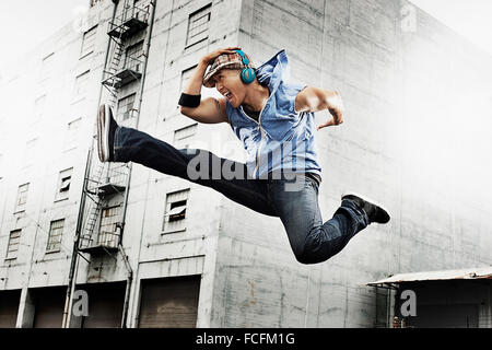 Un giovane uomo che fa un karate kick, una gamba tesa e una gamba piegata fino, indossa gli auricolari. Foto Stock