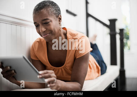 Una donna matura giacente su un divano utilizzando una tavoletta digitale. Foto Stock
