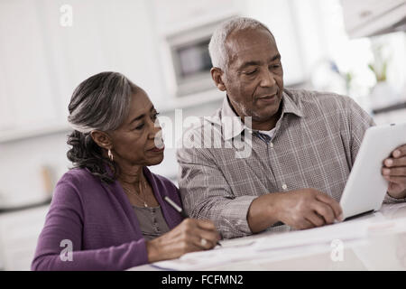 Una coppia senior seduti ad un tavolo a fianco a fianco, utilizzando una tavoletta digitale, guardando lo schermo. Foto Stock