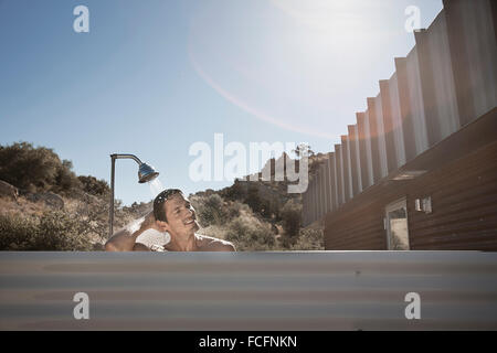 Un uomo che fa la doccia all'aperto sulla terrazza di un basso impatto eco house. Foto Stock