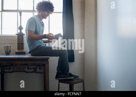 Loft living. Un giovane uomo seduto su una tabella utilizzando una tavoletta digitale. Foto Stock