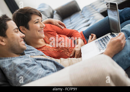 Un uomo e una donna seduta su un divano, guardando lo schermo di un computer portatile. Foto Stock
