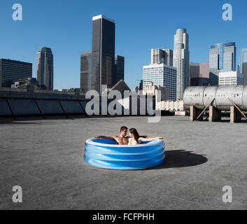 Una coppia di uomo e donna seduta in un piccolo gonfiabile piscina di acqua su una città sul tetto e il raffreddamento. Foto Stock