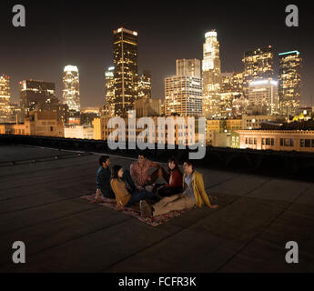 Un gruppo di amici riuniti sul tetto che si affaccia su una città illuminata di notte. Foto Stock