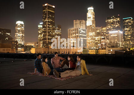 Un gruppo di amici riuniti sul tetto che si affaccia su una città illuminata di notte. Foto Stock