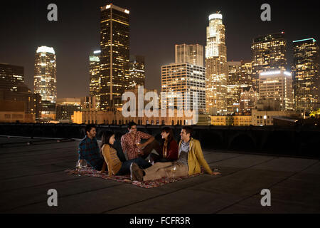 Un gruppo di amici riuniti sul tetto che si affaccia su una città illuminata di notte. Foto Stock