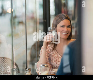 Una donna seduta al tavolo del bar sollevando un bicchiere di vino, sorridente al suo compagno. Foto Stock