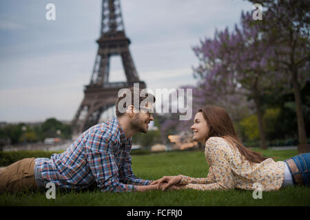 Un giovane sdraiati sull'erba tenendo le mani sotto l'ombra della Torre Eiffel a Parigi. Foto Stock