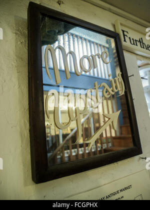 In legno marrone specchio incorniciato con dipinta su lettere corsive di dire di più al piano di sopra con la freccia in corrispondenza di un antico parsimonia store in Hay-on- Foto Stock