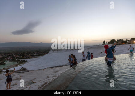 Turistica prendendo le foto in una piscina artificiale di Pamukkale con persone intorno al crepuscolo Foto Stock