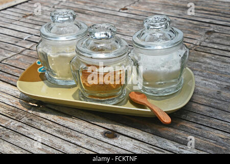 Tre vasi di vetro di zucchero differente, bianco e marrone di canna, sul piattino in ceramica con il cucchiaio di legno sul vecchio vintage tabella di bambù per c Foto Stock