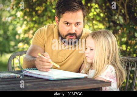 Padre con la figlia nel giardino al tavolo, facendo i compiti in un giorno di estate. Foto Stock