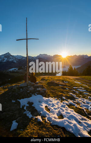 Paio di guardare un tramonto in inverno sulla coperta di neve Glarona montagne in Svizzera da mine antiuomo in punto di vista con una croce latina Foto Stock