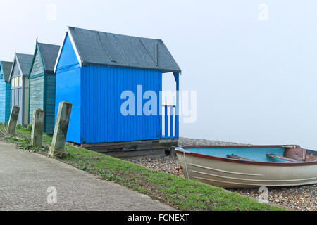 Verde blu cabine in legno e la vecchia barca da pesca da un sentiero in inglese Kentish località balneare di Margate su un nebbioso giorno Foto Stock
