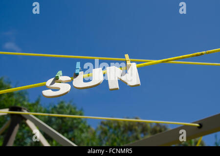 Lettere che formano la parola SOLE appeso da un vestiario con il sole sullo sfondo, immagine concettuale per il sole o il tempo soleggiato Foto Stock