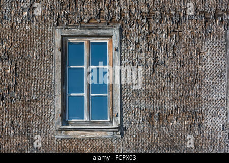 Finestra di reticolo su una facciata weatherboarded di un vecchio, weathered facciata in legno. Vecchio scandole di legno. Foto Stock