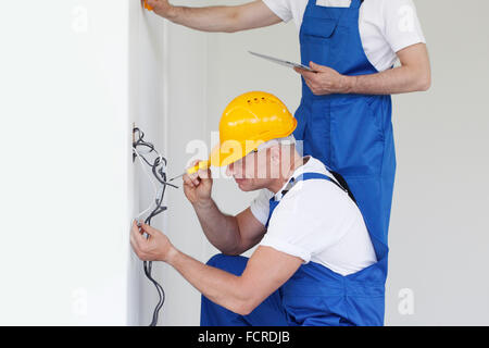 Due costruttori nei caschi che lavora con l'elettricità in ambienti interni Foto Stock