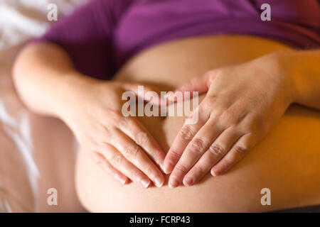 Le mani la sagomatura di un cuore sulla gravidanza della madre ventre bambino Foto Stock