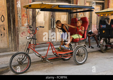 Bambini che giocano su taxi bicicletta, Habana Vieja (l'Avana Vecchia), Cuba Foto Stock