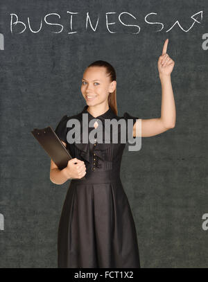 Business donna tenendo un clipboard e punti a chalk-disegnate word business Foto Stock