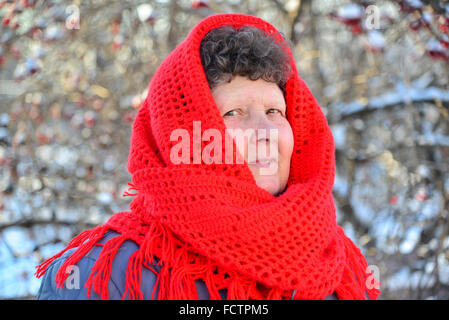 Donna anziana in rosso sciarpa lavorata a maglia sul suo capo all'aperto Foto Stock