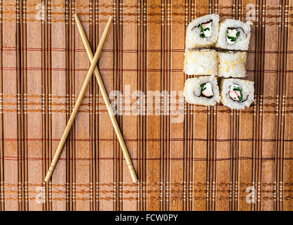Bacchette e sushi roll sul tappetino di bambù. menu sfondo Foto Stock