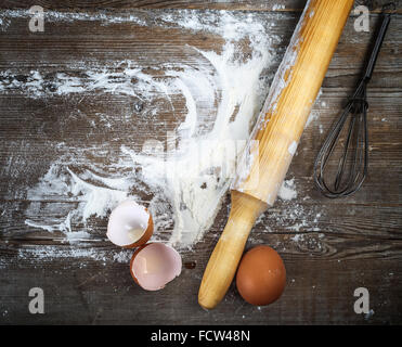 Uova, gusci d'uovo, la farina e il perno di rotolamento su sfondo di legno. Vintage sfondo di cottura. Foto Stock