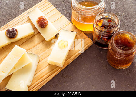 Una composizione di formaggi italiani pecorino fette con marmellate di sapori diversi su un tagliere di legno Foto Stock