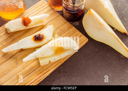 Una composizione di formaggi italiani pecorino fette con marmellate e pere su un tagliere di legno Foto Stock