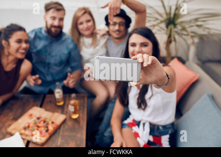 Giovani amici in una parte contraente di adottare qualsiasi autoritratto con smart phone. Focus sul telefono cellulare nella donna la mano. Un gruppo di giovani sit Foto Stock