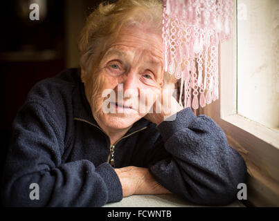 Una donna anziana si siede vicino alla finestra. Foto Stock