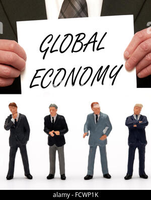 Statuetta in miniatura Business uomini vestiti in abiti con il messaggio economia globale su una scheda che viene tenuto da un uomo in una tuta Foto Stock