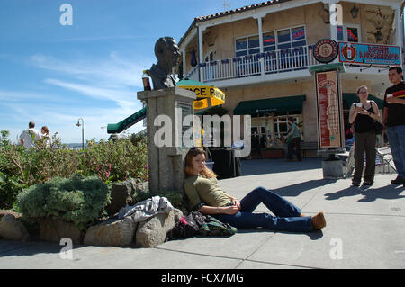 Giovane donna seduta sul marciapiede alla John Steinbeck monumento, Cannery Row, Monterey, California, Stati Uniti d'America Foto Stock