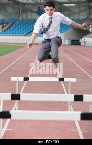 Uomo in business usura saltando ostacoli su una traccia Foto Stock