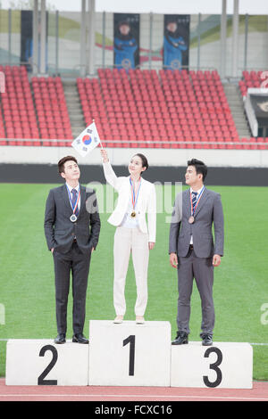 Business donna e due uomini d'affari in piedi sul podio i vincitori e la donna in possesso di una bandiera coreana fino Foto Stock