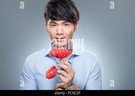 Uomo in camicia blu holding fiori di colore rosso e con lo sguardo in avanti Foto Stock