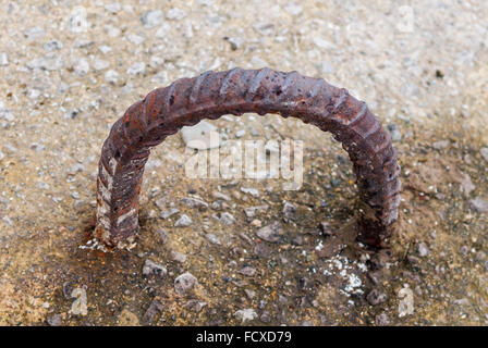 Arrugginita Dirty old metallo rebar loop con entrambe le estremità annegata nel cemento. Foto Stock