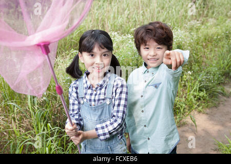 I due ragazzi con lo sguardo in avanti con un sorriso con una farfalla net presso il campo in erba e il ragazzo puntando con il suo dito in avanti Foto Stock