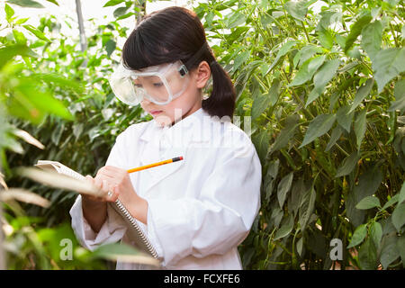 Ragazza in abito bianco e occhiali da laboratorio a scrivere su un notebook circondato da piante Foto Stock