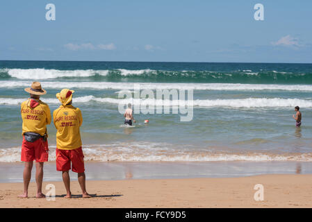 Bagnini sulla spiaggia di Manly, Australia. Nonostante i segni premonitori di una forte surf, due uomini giocano nel surf in Australia il giorno di festa nazionale, guardato con cautela da due bagnini Foto Stock