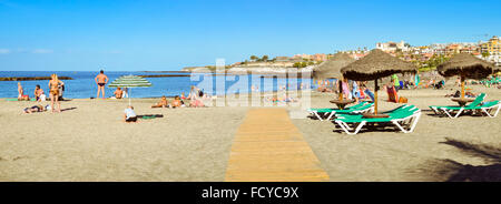 TENERIFE, Spagna - 14 gennaio 2013: la spiaggia di sabbia fine attrezzata con ombrelloni di paglia e lettini, vista dell'El Duque Castello, Costa Adeje, Te Foto Stock