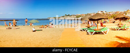 TENERIFE, Spagna - 14 gennaio 2013: la spiaggia di sabbia fine attrezzata con ombrelloni di paglia e lettini, vista dell'El Duque Castello, Costa Adeje Foto Stock